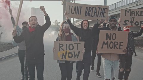Slowmo tracking shot of diverse young people with signs and smoke bombs walking and chanting