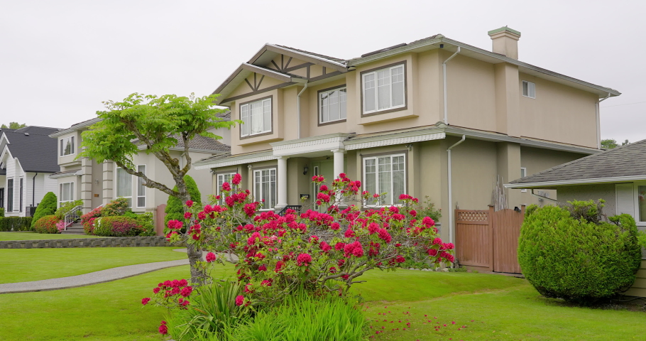 Establishing shot of two story stucco luxury house with garage door, big tree and nice landscape in Vancouver, Canada, North America. Day time on June 2021. ProRes 422 HQ.