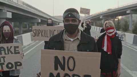 Tilt up portrait shot of young people in face masks standing on highway and holding signs in protest