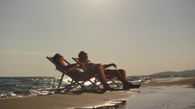 Man and woman laying in beach chairs and relaxing in late afternoon sun. Waves washing sand under loungers. Summer at seaside. - Powered by Shutterstock - Get 15% off with code: PIKWIZARD15
