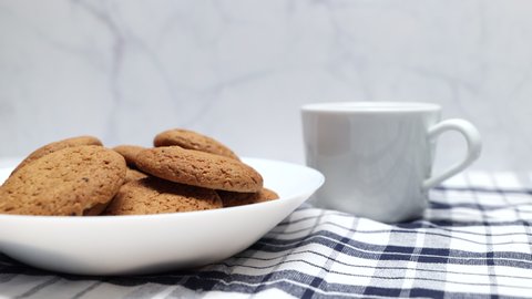 Fresh Brown Oatmeal Cookies In A White Bowl With A White Cup On A Kitchen Towel. The Concept Is A Kind Of White Kitchen With A Mug And Cookies. Slider Shot.
