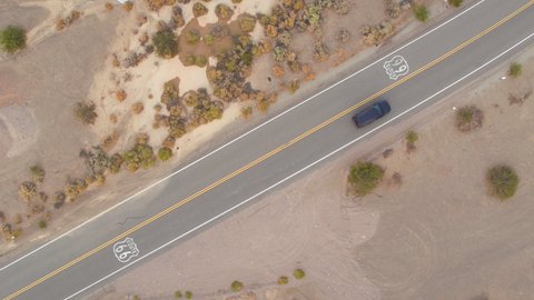TOP DOWN: Flying above Route 66 as the lone tourist car drives along the famous straight highway. Drone point of view of the scenic highway crossing the rugged landscape of rural California, USA.