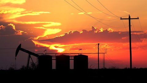 SILHOUETTE: Scenic shot of a pump jack extracting crude oil at a field in Texas on a sunny summer evening. Massive pump jack pumps fossil fuel from the depths of a field in Austin, Texas at sunset.