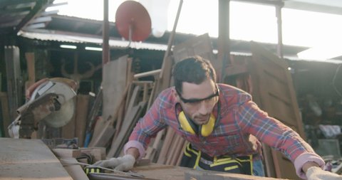 Carpenter woodenworker craft man wearing safety glass and earmuff working in furniture shop using professional cirular saw machine and glinder wood machine blowing saw dust and alignment