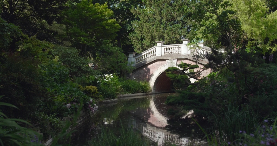 Static view of Parc Monceau with beautiful stone bride across river on summer day in Paris, France.