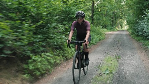 Gravel cycling. Woman riding road bicycle in forest. Cyclist twists pedals on bike along single forest gravel road. Biking adventures. Recreation vacation. Leisure activity. Fitness exercises