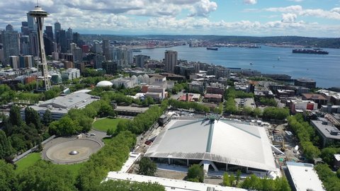 Cinematic 4K aerial drone footage of the Climate Pledge Arena near the International Fountain, Seattle Space Needle at Seattle Center, with Elliott Bay, Port of Seattle in the background