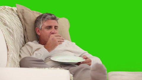 Retired Caucasian man watching tv while he is eating against a green screen