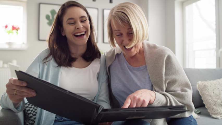 Two woman having fun during looking old photo album together. Shot with RED helium camera in 8K.