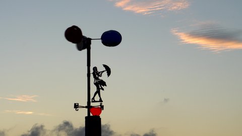 Wind indicator. Rotation of the blades. Vane. Silhouette of a girl with an umbrella. The strength of the wind. Evening time. Clouds in the sky