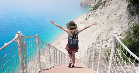 Back view of tourist woman with back pack walking down the stairs at Egremni beach during summer vacation, Lefkada island, Greece.