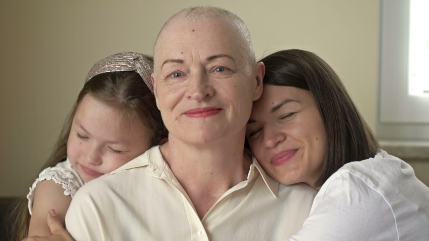 An adult daughter and little granddaughter hug a sad elderly woman who has gone bald after chemotherapy. Love, care and support in the family of a cancer patient. Royalty-Free Stock Footage #1075034387