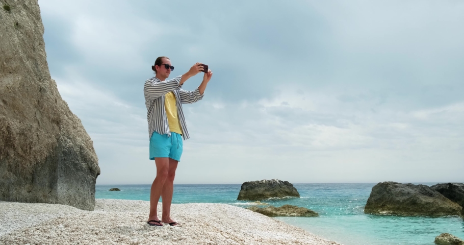 Young tourist man taking pictures of beautiful beach with smartphone.