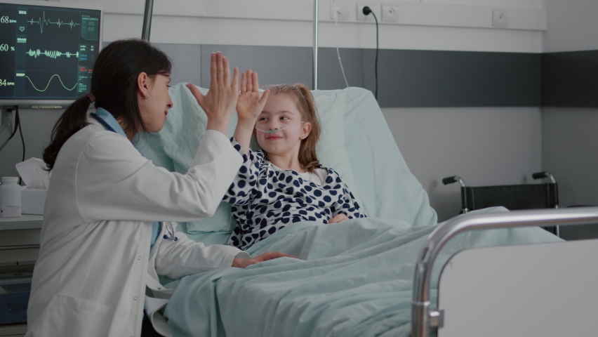 Pediatric woman doctor interacting with sick patient giving high five during clinical consultation in hospital ward. Child lying in bed wearing oxygen nasal tube waiting for medication treatment Royalty-Free Stock Footage #1075036892