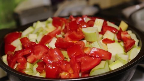 A woman's hand puts vegetables into a black pan, throwing zucchini and carrots, tomatoes, peppers. Cooking food at home. Preparation for frying