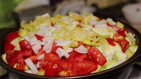A female hand closes the lid in a frying pan, frying zucchini and carrots, tomatoes, peppers. Cooking food at home. Preparation for frying