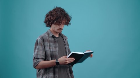 The charismatic young man, thoughtfully making notes, thinks, and when an idea comes to him, he writes it down in the diary. Isolated on a turquoise background. Concept of life. People's emotions. 4k