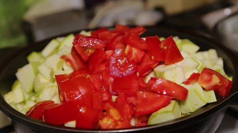 A woman's hand puts vegetables into a black pan, throwing zucchini and carrots, tomatoes, peppers. Cooking food at home. Preparation for frying