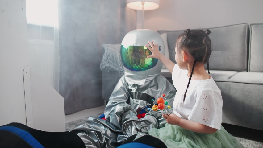 Asian kids play in the living room at home, a boy in an astronaut costume sitting on the floor with her sister, kids playing with a toy model of the solar system, 4k slow motion.