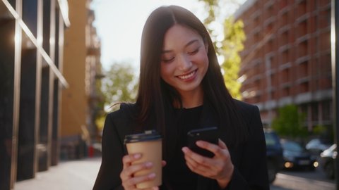 Amazing attractive chinese mixed-race young business woman spending office break outside, drinking takeaway coffee and browsing social media on smartphone.