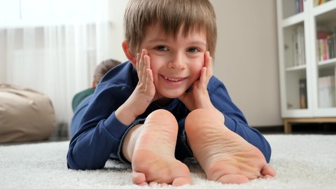 Portrait of happy smiling boy lying on mother's feet and looking in camera. Family having fun and playing together.