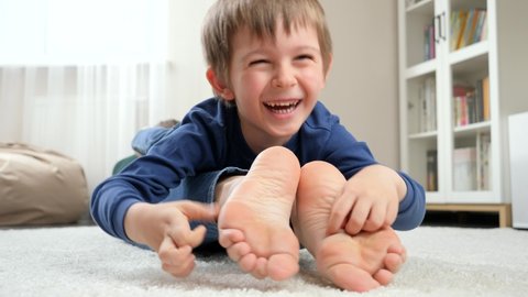 Funny laughing boy lying on mother and tickling her feet. Family having fun and playing together.