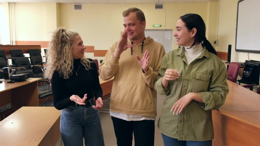 Two girls and a guy are talking in sign language. Three deaf students chatting in a university classroom. | Shutterstock HD Video #1075045100