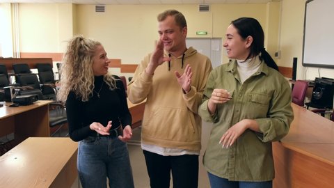 Two girls and a guy are talking in sign language. Three deaf students chatting in a university classroom.