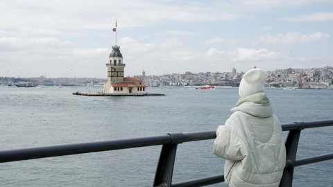Tourist woman looking to Maiden Tower in Bosporus on observation deck in Istanbul city, Turkey. Young female traveler sightseeing to Kiz Kulesi Tower