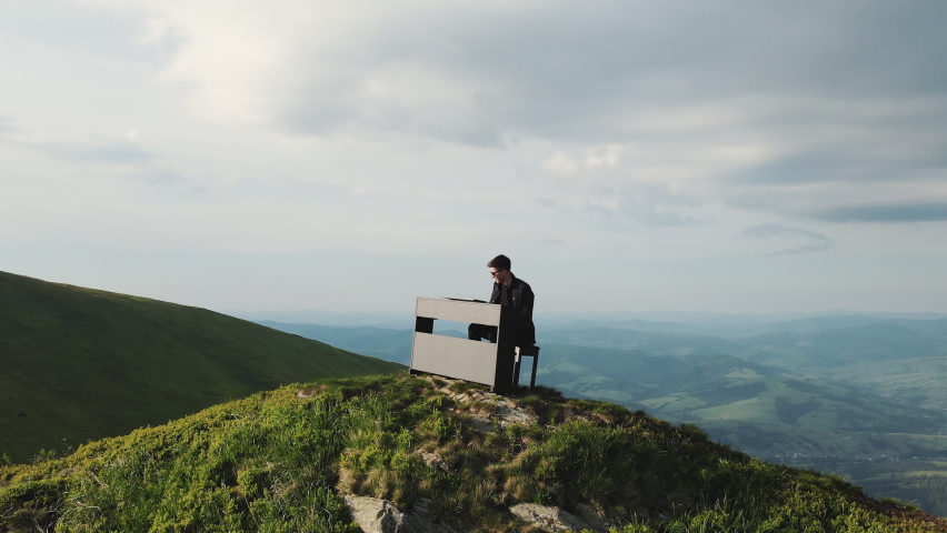 Aerial view of pianist plays on grand piano in the mountains. Man two hands plays gentle classical music on a grand piano on nature. Professional pianist. Man touches fingers on keys Royalty-Free Stock Footage #1075047011