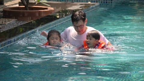 Happy asian family with inflatable or life jacket playing in swimming pool at hotel enjoying summer vacation. young father and  daughter and son relaxing in swimming pool together outdoors