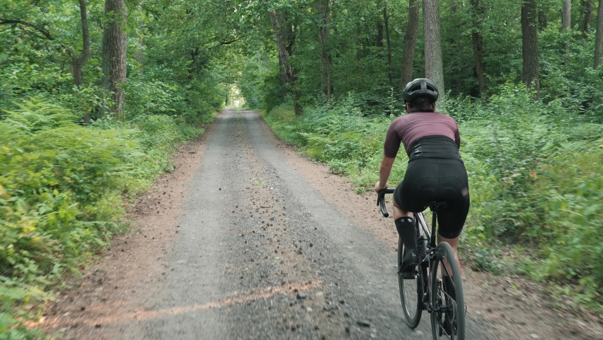 Cyclist riding bicycle in forest. Woman rides gravel road in national park or forest. Female riding beautiful epic forest landscape. Cycling biking outdoor. Leisure activity. Recreation vacation