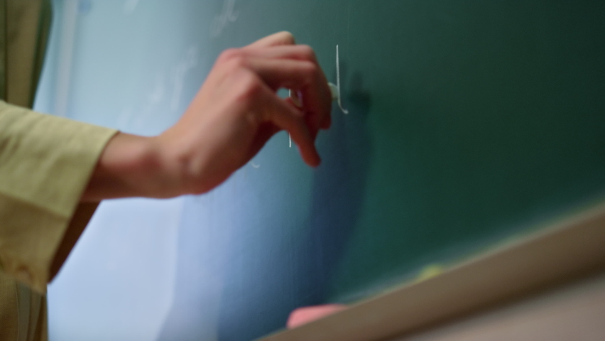 Female teacher drawing on blackboard in classroom. Schoolteacher hand writing English words on chalkboard during lesson. Closeup woman arm putting chalk on shelf in auditorium