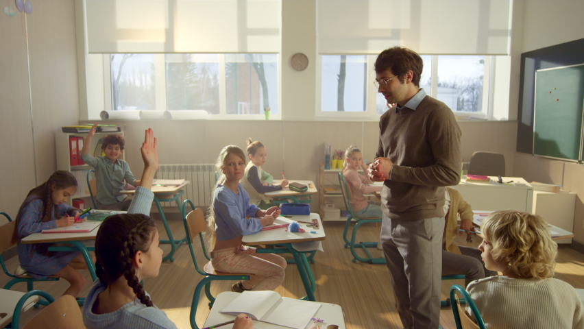 Crane shot of smiling teacher asking questions to kids in school class. Clever schoolchildren raising hands at lesson in classroom. Mixed race pupils answering questions of schoolteacher at school Royalty-Free Stock Footage #1075050596
