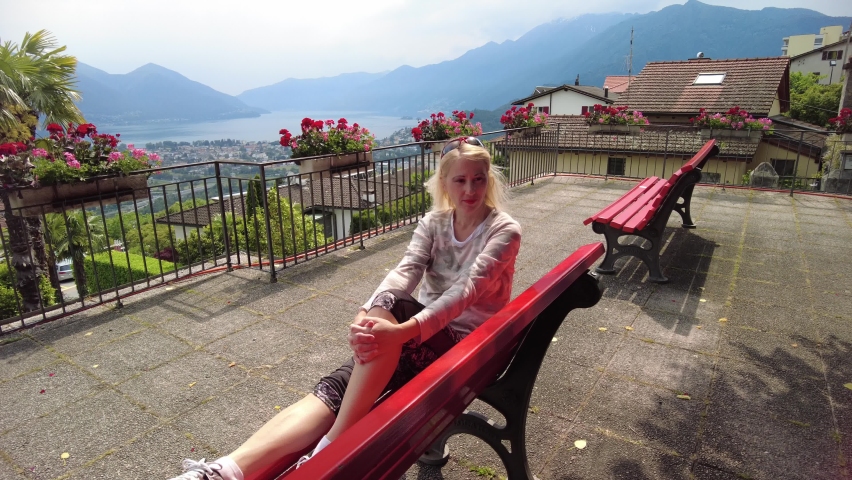 Woman sitting on top of Lake Maggiore in Switzerland. Swiss bench at aerial view lookout from Orselina town of Locarno and Ascona on Cardada mount. Lake Maggiore skyline from Bre mount, Ticino Canton.