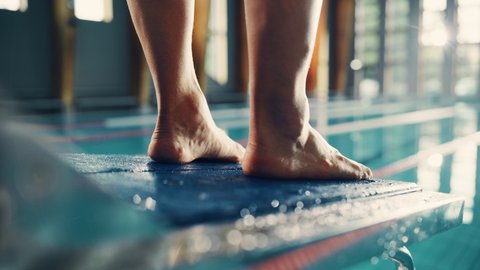 Swimming Pool: Professional Swimmer Steps on Starting Block. Overcoming Fear, Determined Athlete Ready to Set New Record on a Championship. Stylish Cinematic Focus on Legs. Bokeh Close-up