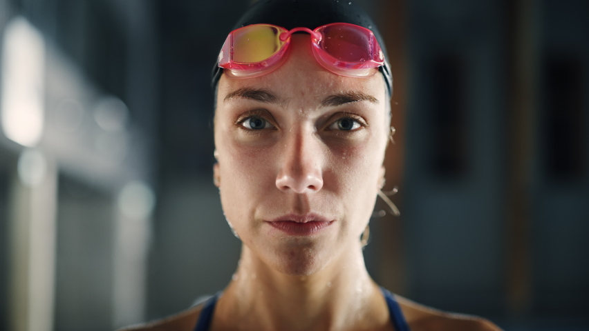 Beautiful Professional Female Swimmer in Swimming Pool, Wearing Cap, Looks Confidently at the Camera, Puts on Glasses, Ready to Win the Championship, Set New World Record. Cinematic Close-up Portrait Royalty-Free Stock Footage #1075052324