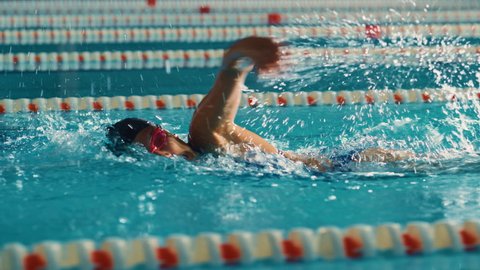 Successful Female Swimmer Racing, Swimming in Swimming Pool. Professional Athlete Determined to Win Championship using Front Crawl Freestyle. Colorful Cinematic Shot. Side View Tracking Slow Motion