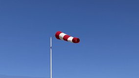 Windsock flutters in a strong wind showing wind direction and speed against perfect blue sky on clear summer day.