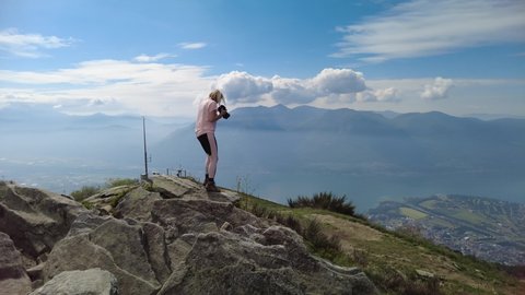 Photographer woman taking pictures with camera on top of Cardada-Cimetta mount in Switzerland. Skyline from Swiss cable car of Locarno on Cardada mount. Lake Langensee cityscape in Ticino.