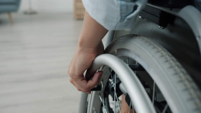 Close-up slow motion of woman's hand moving wheelchair indoors at home while female paraplegic is busy with domestic activities. Disability and mobility concept. Royalty-Free Stock Footage #1075060328