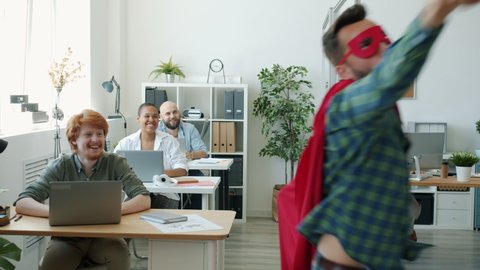 Funny young man in super hero costume is running in office doing high-five with colleagues wearing red cape and mask