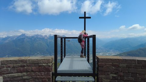 SLOW MOTION: Backpacker photographer woman taking pictures with camera on Tamaro mount cross platform in Switzerland. Swiss panorama on Foppa alp in Ticino canton. Top of Rivera station of cable car.