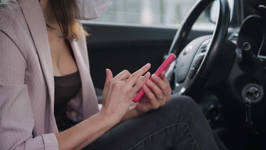 Woman car passenger in mask surfing the internet and browsing social media while waiting for the driver