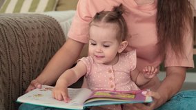 Childcare at Home, Child Protection, New Life, Leisure with Baby. Mom reads a book to the kid while sitting on the floor in the bedroom - Powered by Shutterstock - Get 15% off with code: PIKWIZARD15