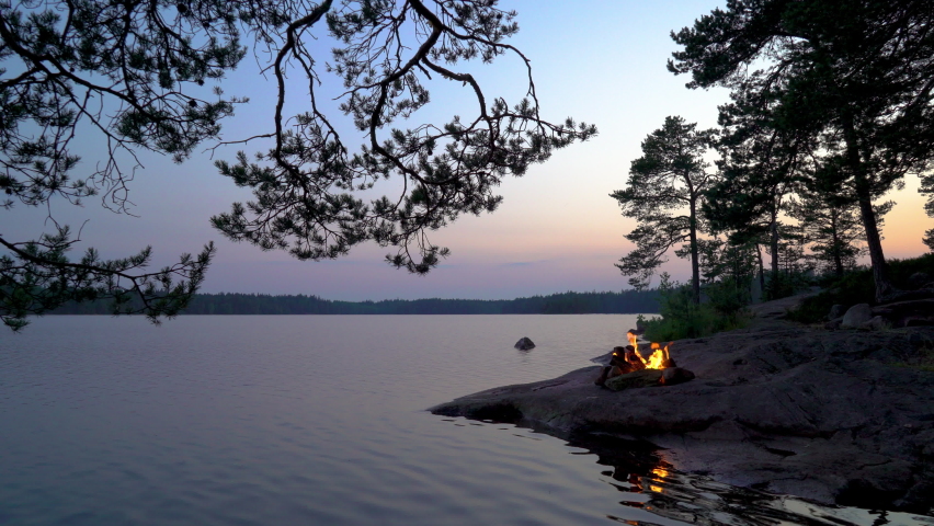 A bonfire burning in a forest on the shore of a lake at midnight on the Summer Solstice. Summer White Night on the eve of Midsummer Day in Finland. Sound of campfire and wildlife, birdsong Royalty-Free Stock Footage #1075071857
