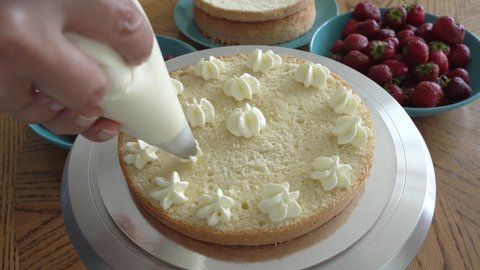 Caucasian woman's hand decorates cake squeezes cream out of pastry bag on rotating round stand