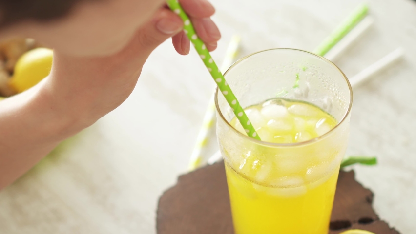 Yellow soda with ice in a tall glass. A girl without a face quenches her thirst, drinks a cocktail through a cocktail tube. A large glass of chilled tropical drink with a paper straw on a hot day.
 Royalty-Free Stock Footage #1075077383