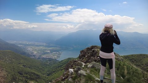 Photographer woman taking pictures with camera on top of Cardada-Cimetta mount in Switzerland. Skyline from Swiss cable car of Locarno on Cardada mount. Lake Langensee cityscape in Ticino.