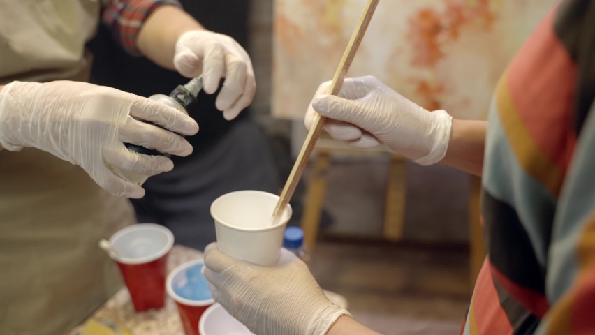 Women artists are mixing acrylic paint in the plastic cup. Adding glue. Artistic collaboration in workshop.